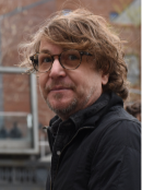 a man with eyeglasses standing outside wearing a black jacket