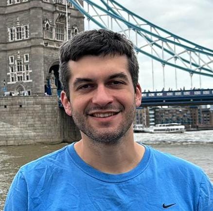 man in blue shirt smiling and standing in front of a bridge