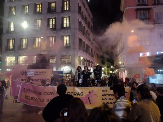 Protest in Valencia with people holding banners and signs, accompanied by smoke in the background.