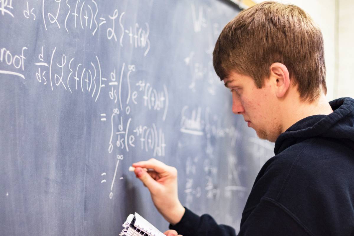 A high schooler solving a math problem on a chalk board